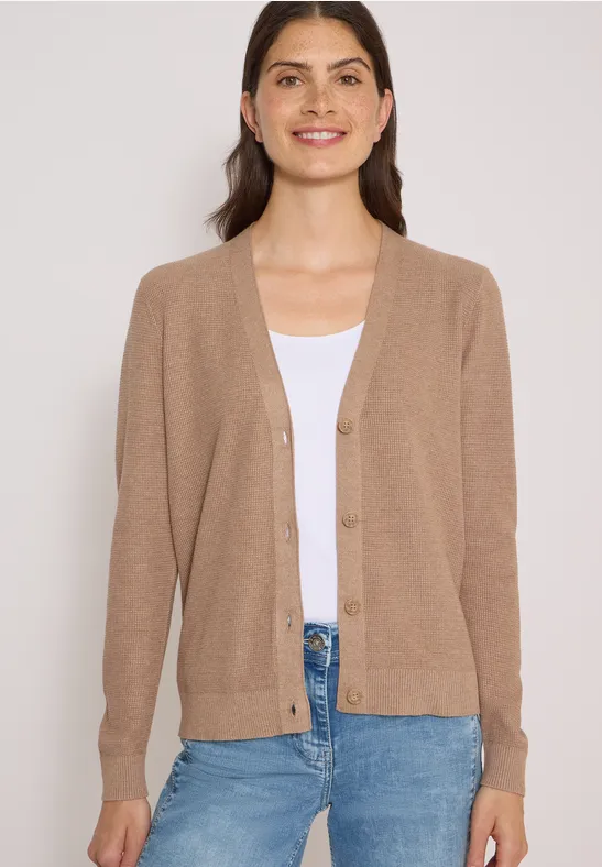 Frau trägt beigen Cardigan, weißes Top und Jeans