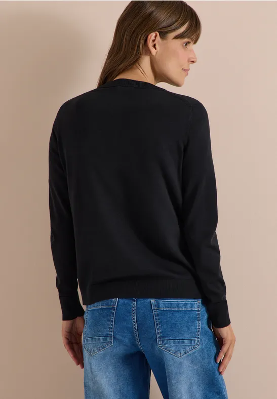 Rückansicht einer Frau in schwarzem Pullover und blauen Jeans vor neutralem Hintergrund