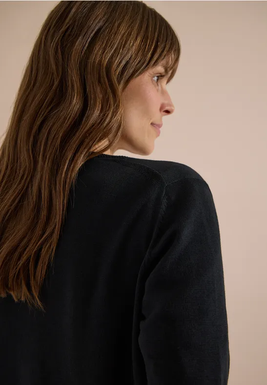 Seitliche Ansicht einer Frau mit langen, welligen Haaren und schwarzem Pullover.