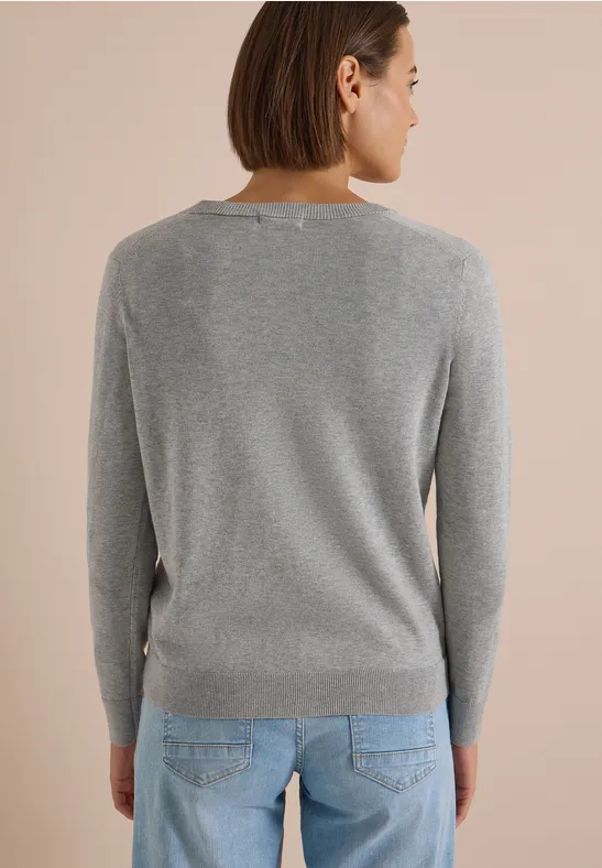 Rückenansicht einer Person mit grauem Pullover und blauer Jeans vor hellem Hintergrund.