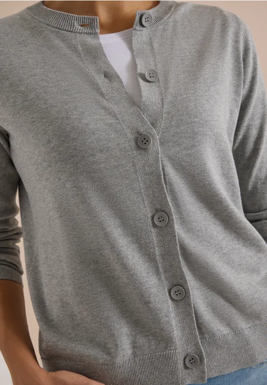Damenstrickjacke in Grau mit Knopfleiste, Rundhals und langem Ärmel, darüber ein weißes T-Shirt.