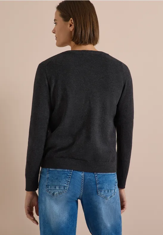 Rückansicht einer Frau in schwarzem Pullover und blauen Jeans vor hellem Hintergrund.