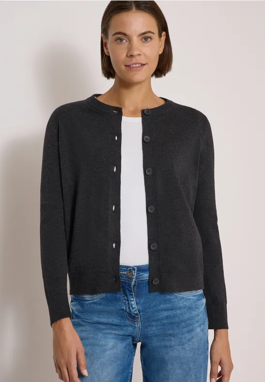 Eine Frau trägt einen schwarzen, knöpfbaren Cardigan über einem weißen Shirt und blaue Jeans.