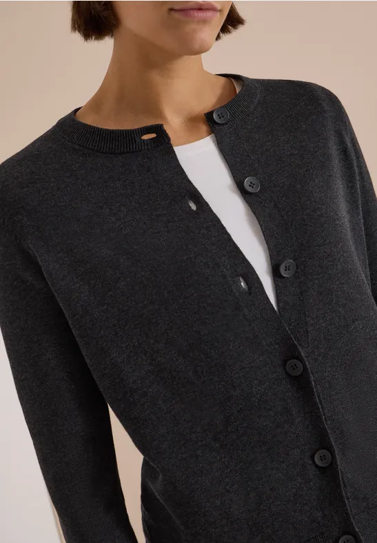 Eine dunkelgraue Strickjacke mit Knopfleiste, die über einem weißen Top getragen wird.