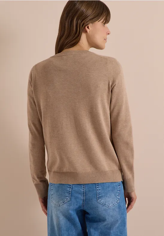 Eine Frau steht mit dem Rücken zur Kamera und trägt einen beigen Pullover und blaue Jeans.