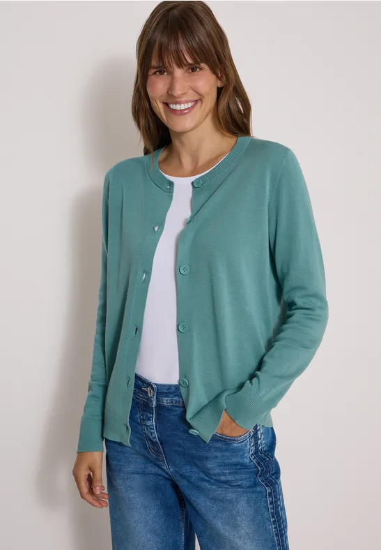 Lächelnde Frau in grünem Cardigan, weißem Shirt und Jeans.