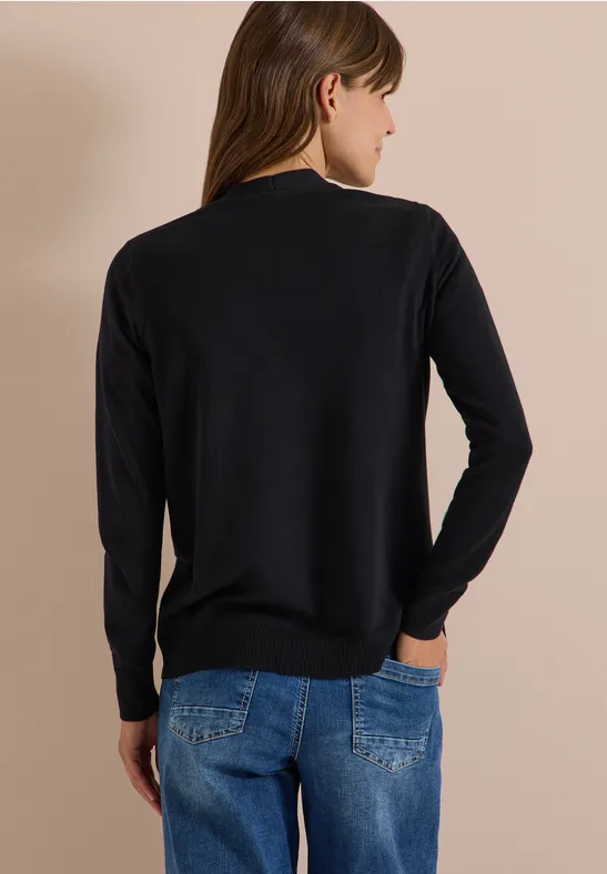 Frau von hinten in schwarzem Pullover und blauen Jeans vor beigem Hintergrund.