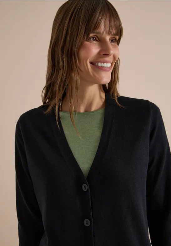 Eine lächelnde Frau mit braunen Haaren trägt einen schwarzen Cardigan und ein grünes Shirt.
