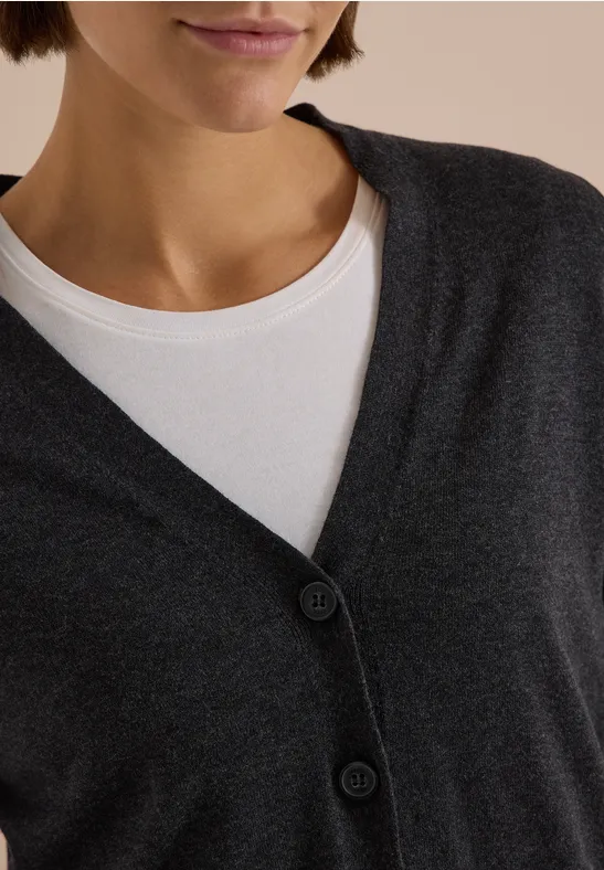 Nahe Ausschnitt: Weißes Rundhalsshirt unter dunkelgrauer, geknopfter Strickjacke.