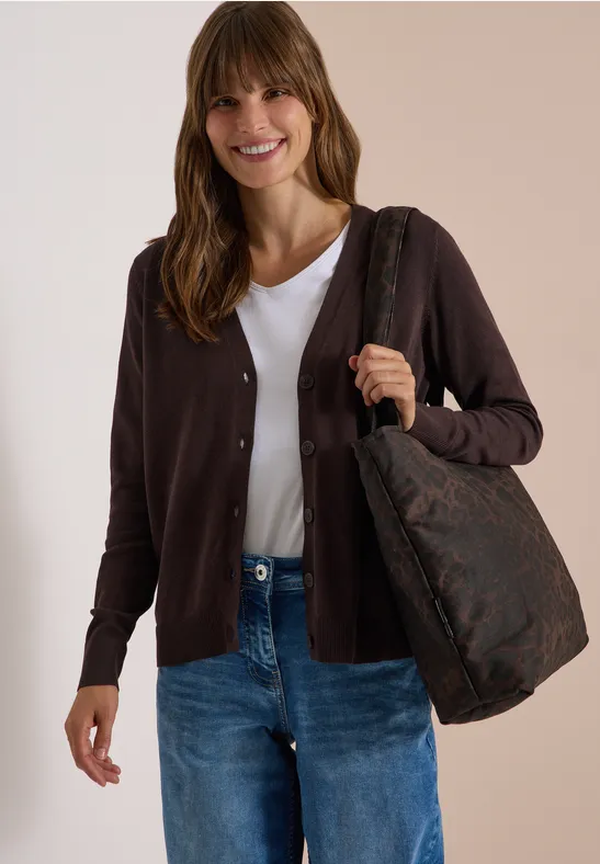 Frau trägt weiße Bluse, dunkelbraune Strickjacke, blaue Jeans und eine gemusterte braune Umhängetasche.