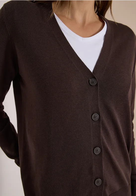Brauner Cardigan mit V-Ausschnitt und fünf Knöpfen über weißem Shirt.