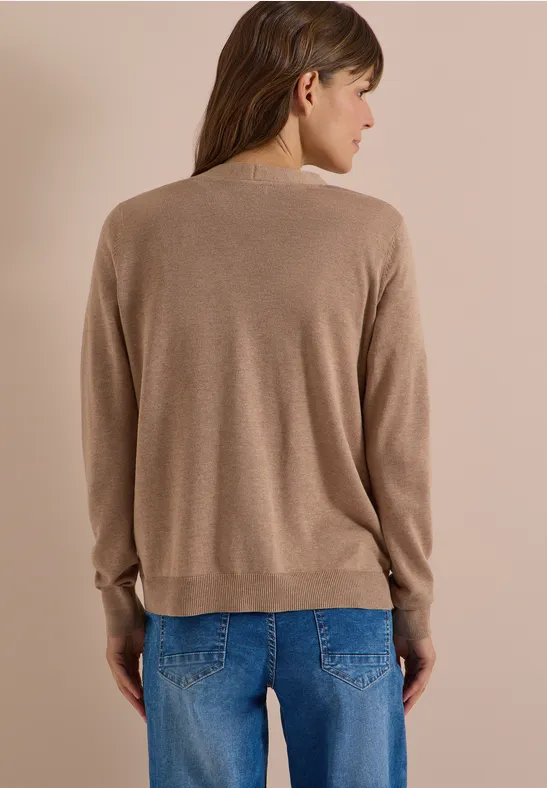 Frau von hinten in beigem Pullover und blauen Jeans vor neutralem Hintergrund
