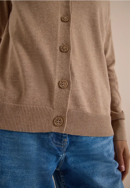 Beiger Cardigan mit Knöpfen kombiniert mit blauen Jeans.