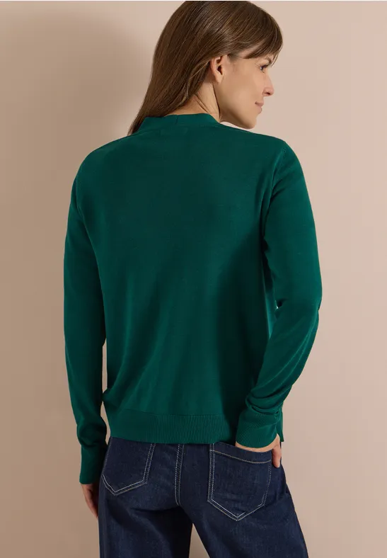Rückansicht einer Frau mit braunen Haaren, die einen grünen Pullover und Jeans trägt.