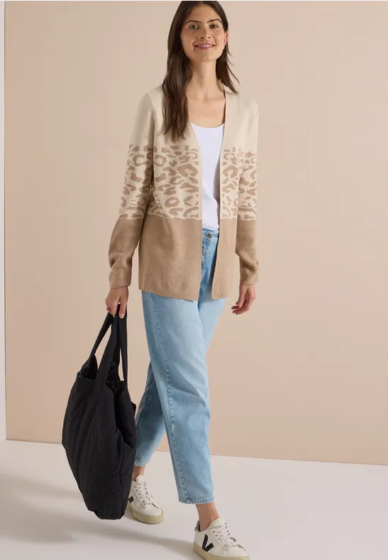 Modell in beiger, Leo-Print-Strickjacke, weißem Top, hellblauen Jeans, weißen Sneakern und großer schwarzer Schultertasche.