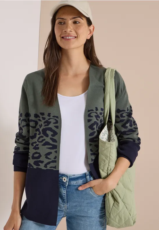 Frau in Cap, weißem Top, zweifarbigem Cardigan mit Leopardenprint, Jeans und gesteppte Tasche.