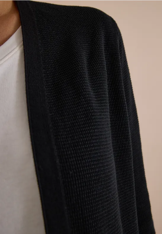 Schwarz gestrickter Cardigan über weißem T-Shirt, nur Oberkörper sichtbar.