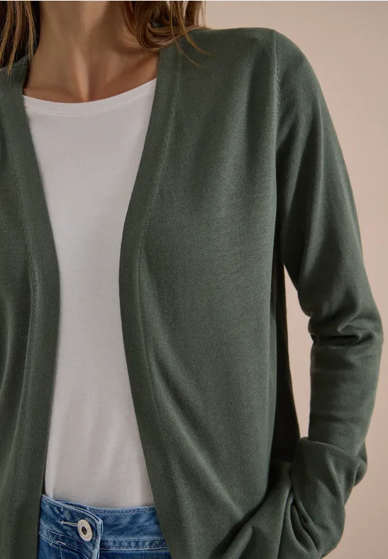 Eine Person trägt einen olivgrünen Cardigan über einem weißen T-Shirt.