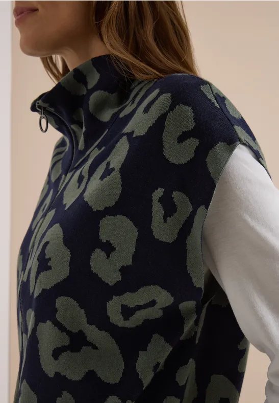 Frau trägt marineblauen, grün gemusterten Ärmellosen Pullunder über weißem Langarmshirt.