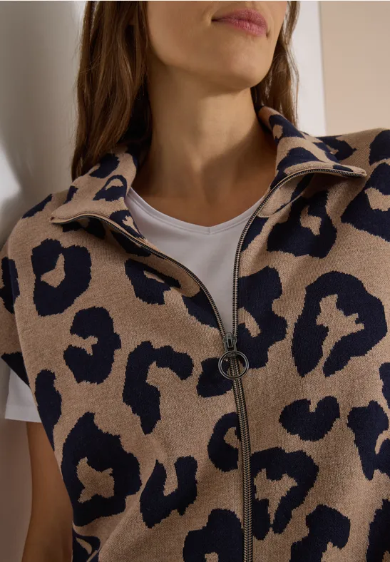 Eine Frau trägt eine beiger Leoparden-Strickjacke mit Reißverschluss und ein weißes T-Shirt.