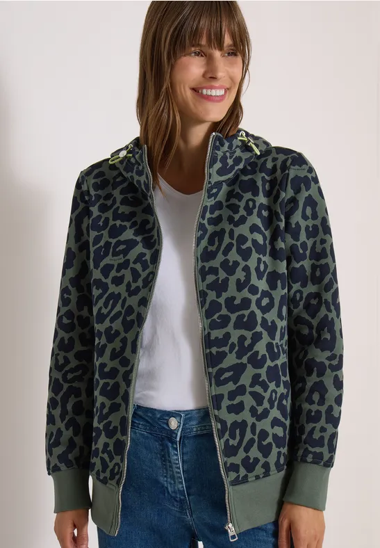 Femme en veste bomber verte à motif léopard noir, tee-shirt blanc et jean.