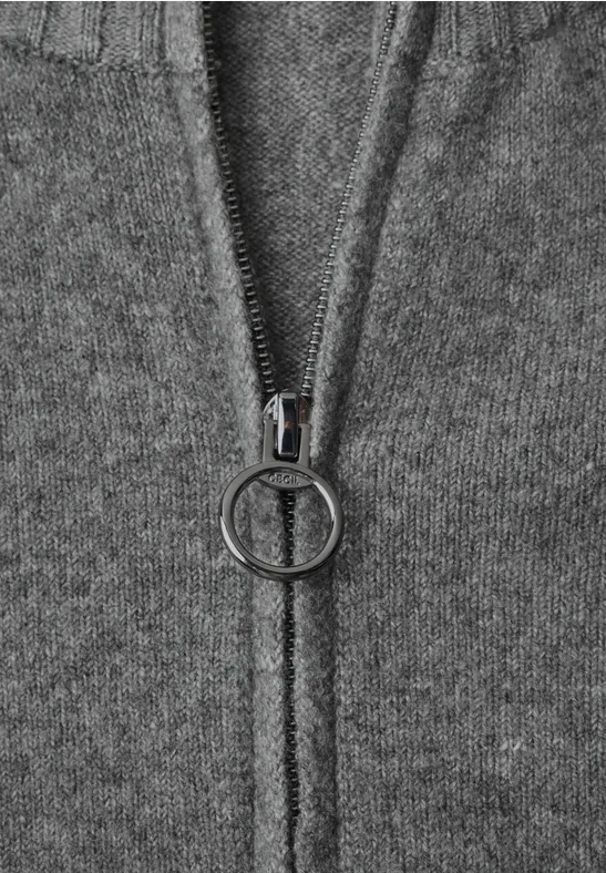 Detail eines grauen Strickstoffs mit Metallreißverschluss und rundem Zipper-Anhänger.