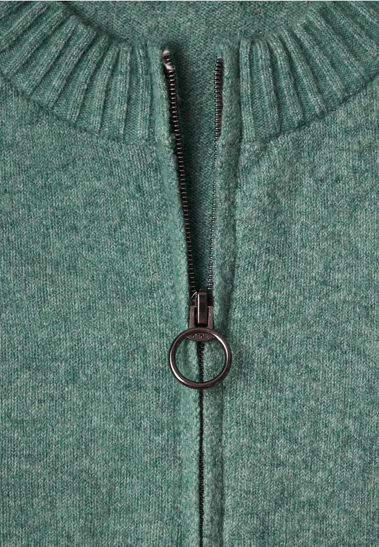 Grüner Strickpullover mit hohem Kragen und Reißverschluss mit rundem Zipper-Anhänger.