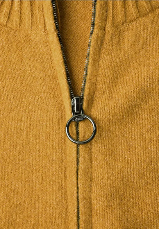 Nahaufnahme eines senfgelben Strickpullovers mit mittig geschlossenem Reißverschluss und rundem Ringanhänger