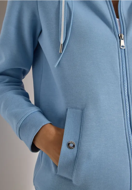 Pastellblauer Kapuzenpullover mit Reißverschluss und seitlicher Tasche, in die die Hand gesteckt ist.