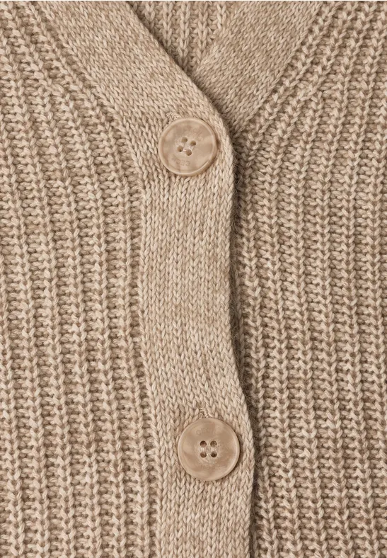 Nahaufnahme eines beigen, grob gestrickten Cardigans mit zwei Knöpfen aus Holz.