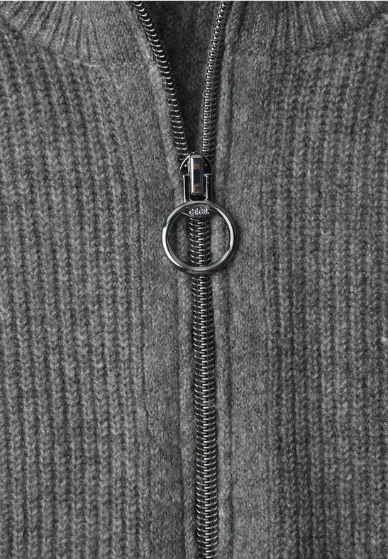 Nahaufnahme eines grauen Strickpullovers mit Reißverschluss und rundem Zipper-Anhänger.