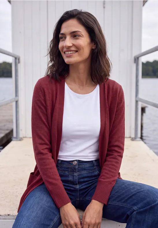 Frau steht entspannt auf einem Steg, trägt roten Cardigan und Jeans.