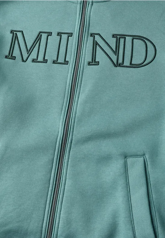 Nahaufnahme eines türkisfarbenen Kapuzenpullovers mit Reißverschluss und dem aufgedruckten Schriftzug „MIND“.