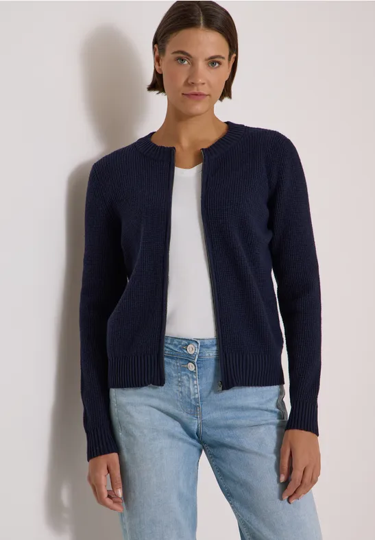 Femme en cardigan bleu marine, top blanc et jean sur fond clair.