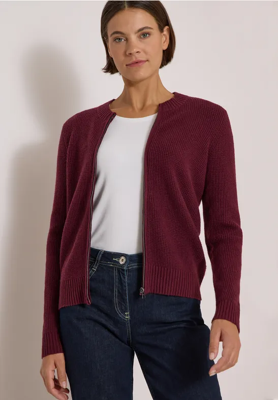 Une femme porte un cardigan bordeaux, un t-shirt blanc et un jean bleu.