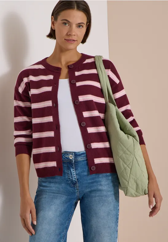 Femme en cardigan rayé, jean et sac matelassé vert.