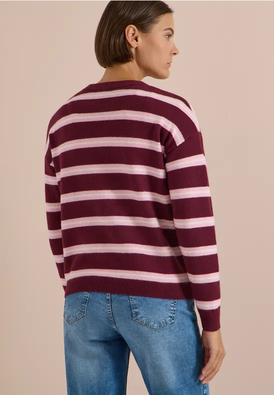 Femme portant un pull à rayures bordeaux et blanc et un jean, vue de dos sur fond clair.