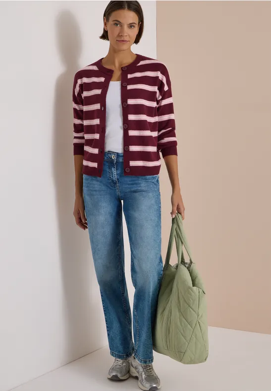 Femme en cardigan rayé, jean bleu, baskets et sac matelassé vert à la main.