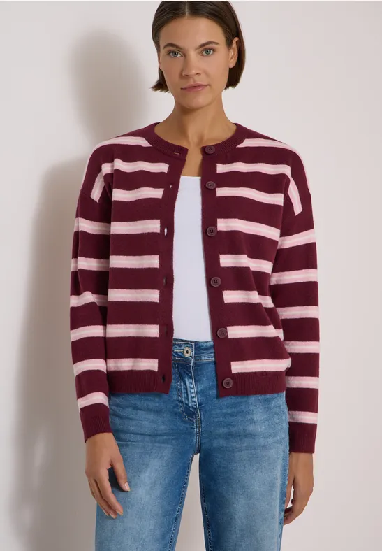 Femme portant un gilet rayé bordeaux et rose, t-shirt blanc dessous, jeans et coupe simple.