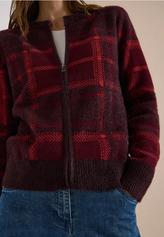 Rotes kariertes Strick-Cardigan mit Reißverschluss über weißem Shirt und blauen Jeans.