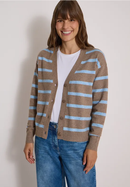 Fröhliche Frau trägt beigen Cardigan mit hellblauen Streifen, weißes Shirt und blaue Jeans.