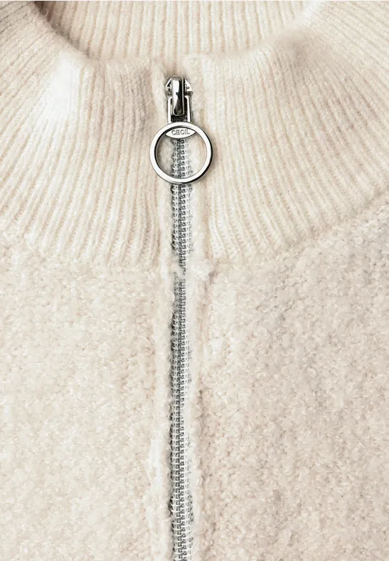 Cremefarbener Grobstrickpullover mit Stehkragen und silbernem Ringzipper.