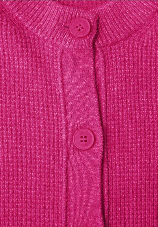 Close-up van een felroze gebreid vest met ribbelpatroon en twee bijpassende knopen