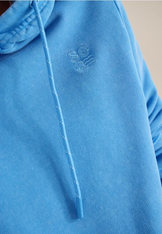 Gros plan d'un sweat à capuche bleu avec cordon de serrage et petit logo brodé sur la poitrine.