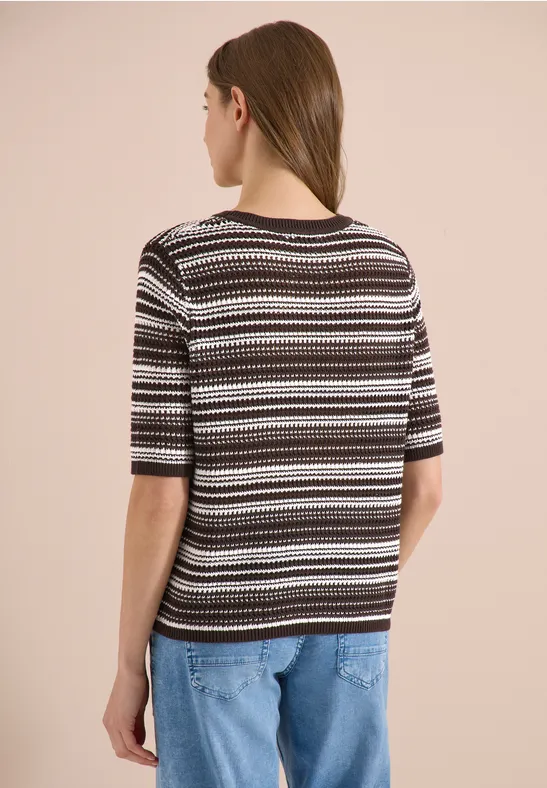 Frau von hinten in kurzärmligem Strickshirt mit schwarzen, weißen und braunen Streifen und lockeren Jeans.