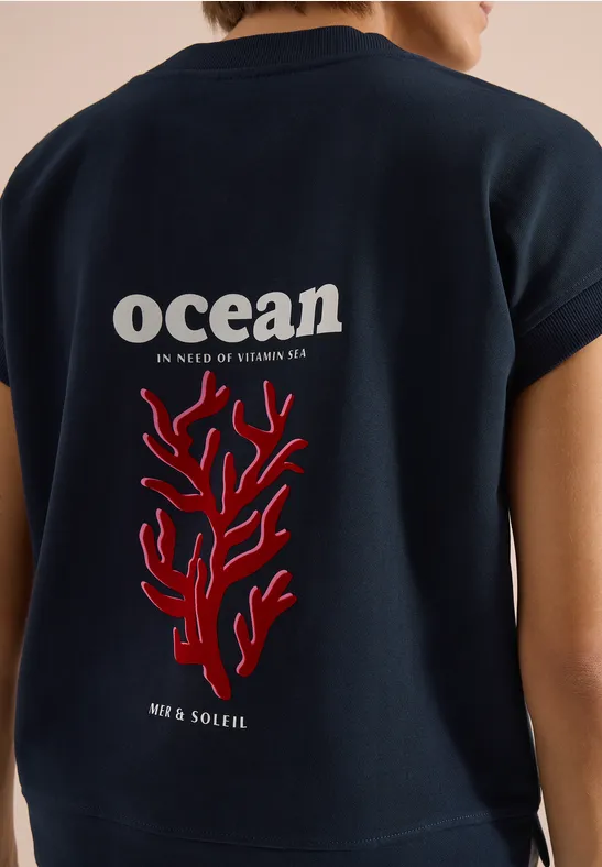 Dunkelblaues Shirt mit Aufdruck 'ocean' und rotem Korallenmotiv am Rücken.