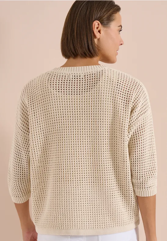 Vrouw van achteren in een losse, beige opengewerkte trui met driekwartmouwen.