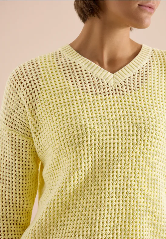 Close-up van een persoon in een gele, losgebreide V-hals trui met open structuur.