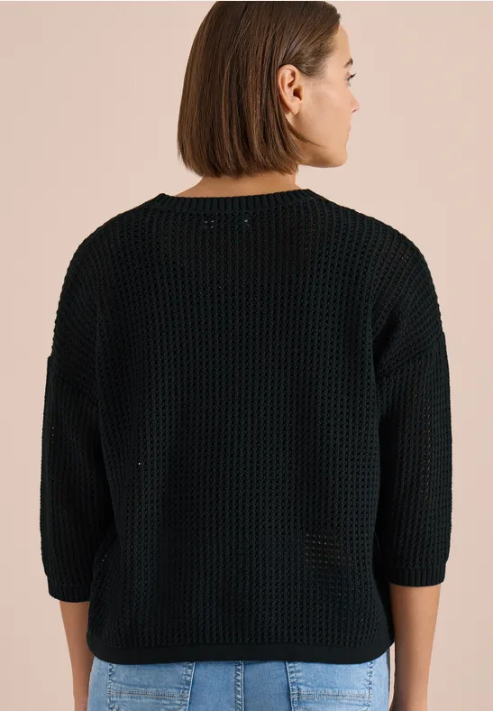 Achteraanzicht van een persoon in een zwarte grofgebreide trui met driekwartmouwen voor een beige achtergrond