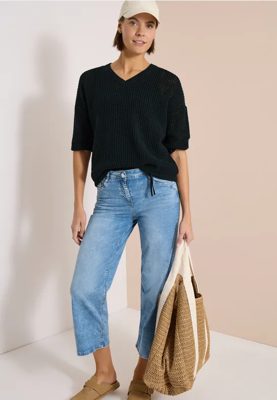 Vrouw in casual outfit: zwarte t-shirt, lichtblauwe cropped jeans en een gevlochten shopper.